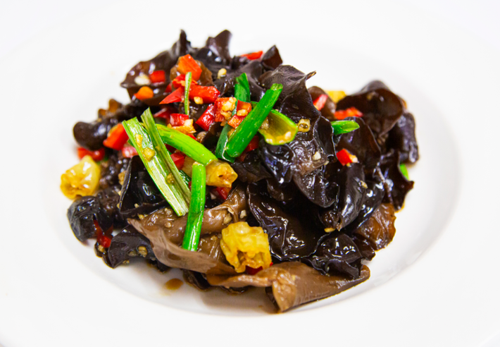Black fungus stir-fry topped with green onions and red chilies on a white plate