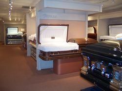 Coffins displayed in a funeral home showroom, including a white-lined open casket in the foreground.