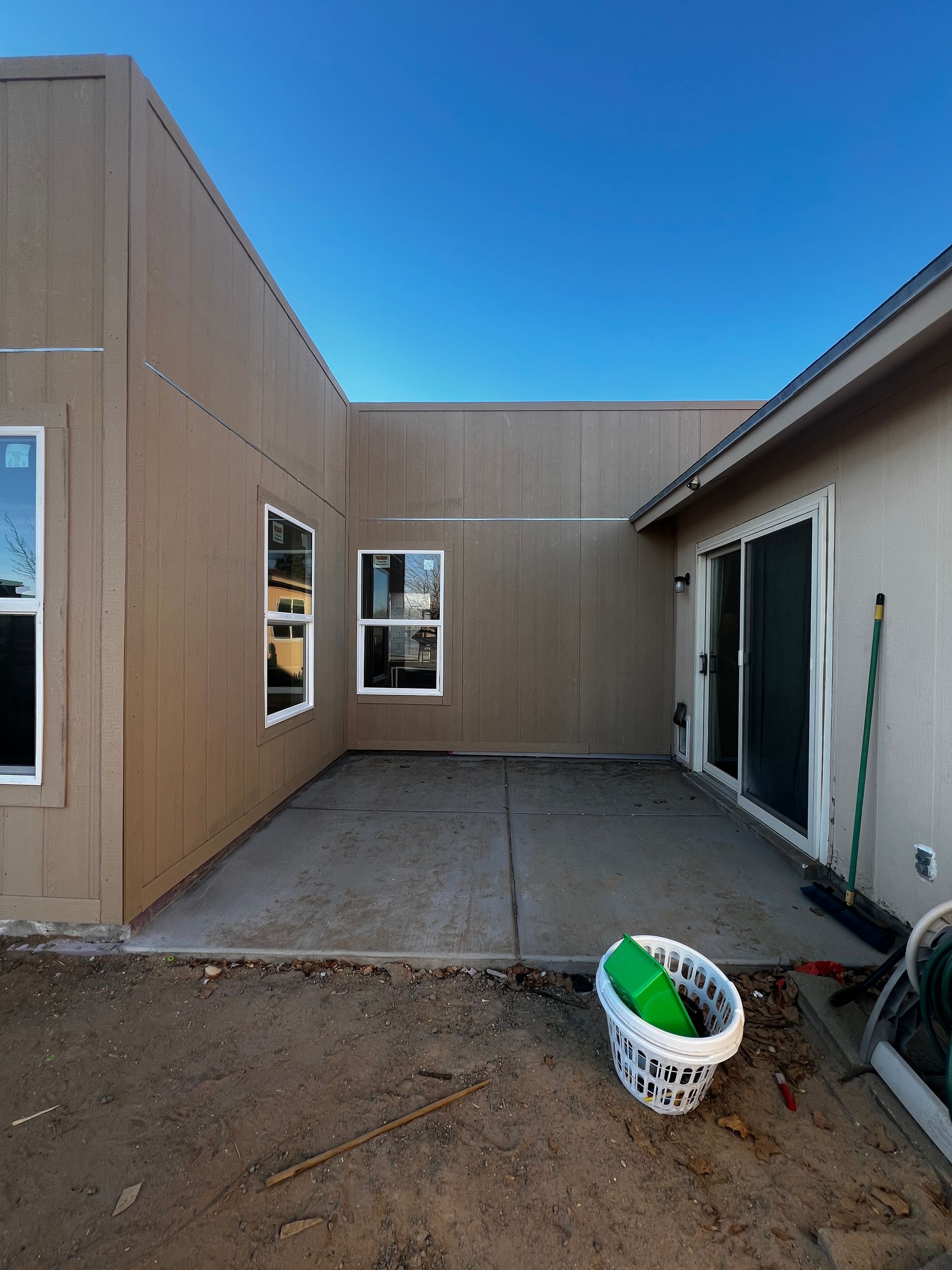 White stucco building with a dark door, beneath a brown awning, and a concrete ramp.
