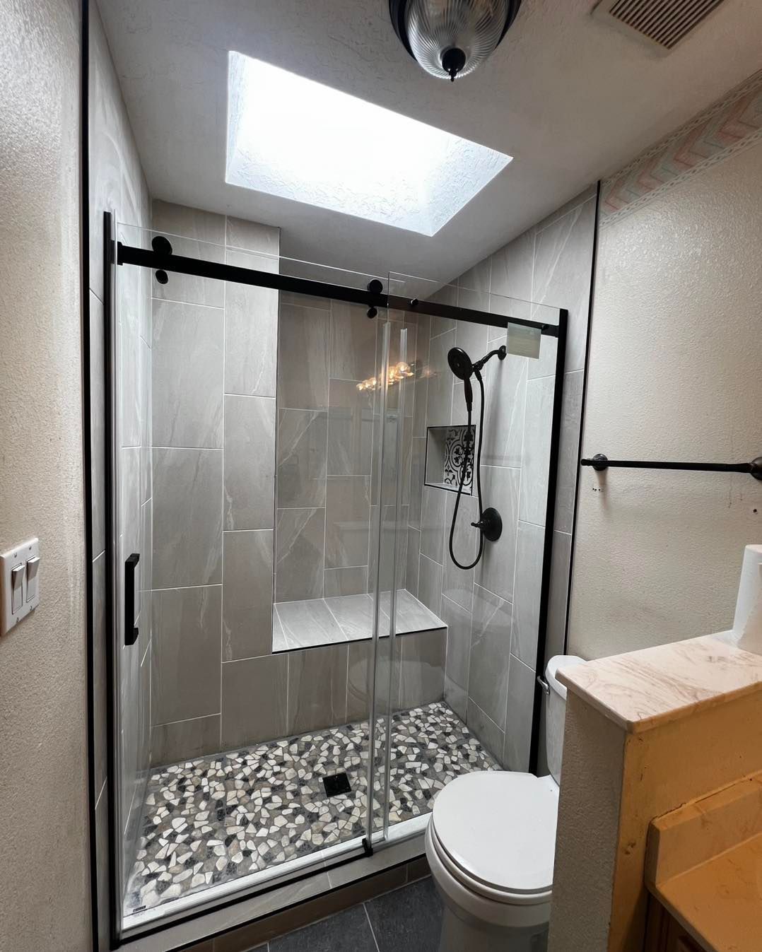 Modern bathroom with a glass shower enclosure, a skylight, and pebble floor.