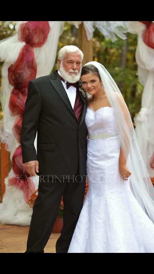 Bride in white gown and older man in black suit posing together at a wedding ceremony
