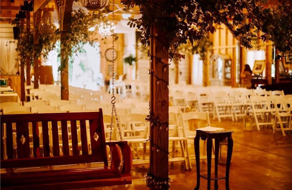 Warmly lit outdoor café seating with benches, hanging greenery, and rows of white chairs at night