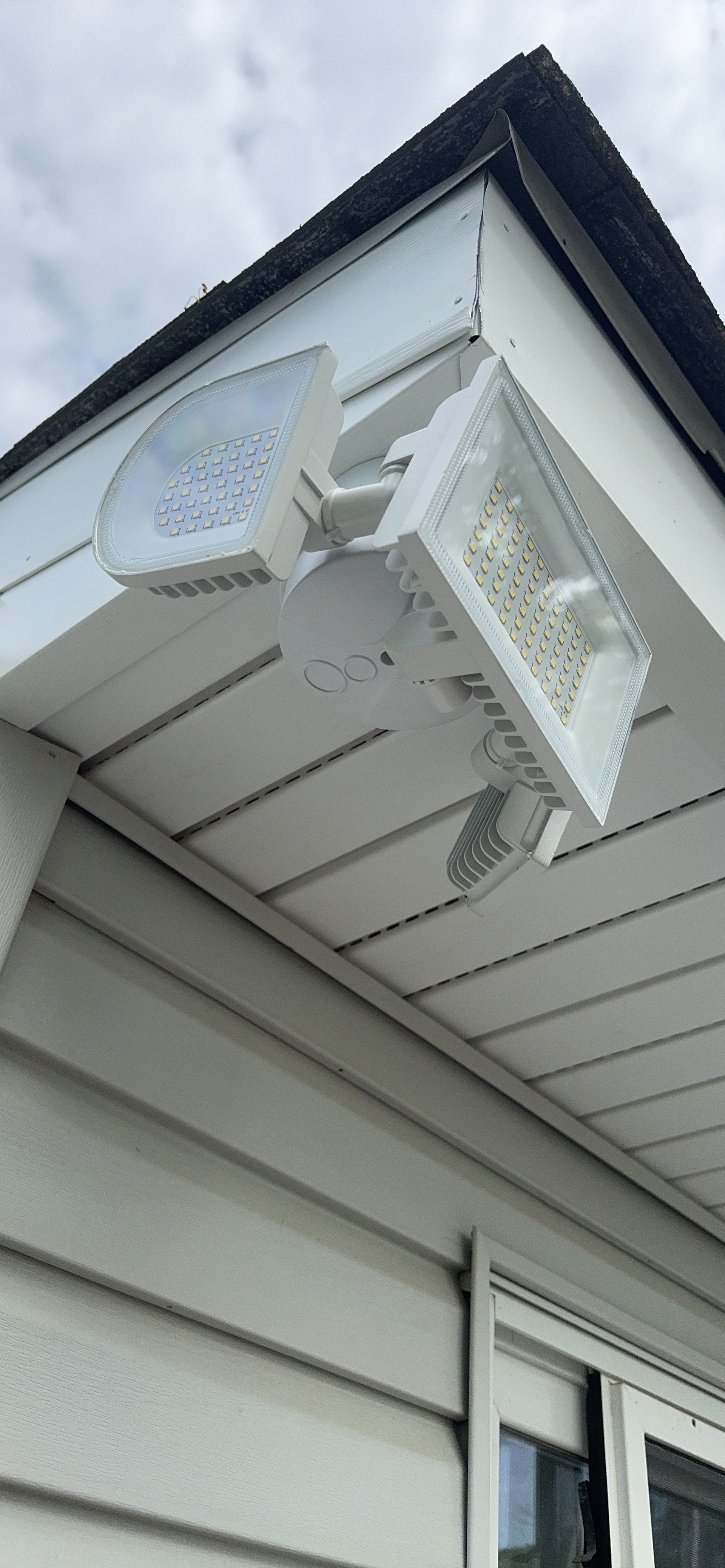 White security camera mounted under a house eave, angled downward beside a window.