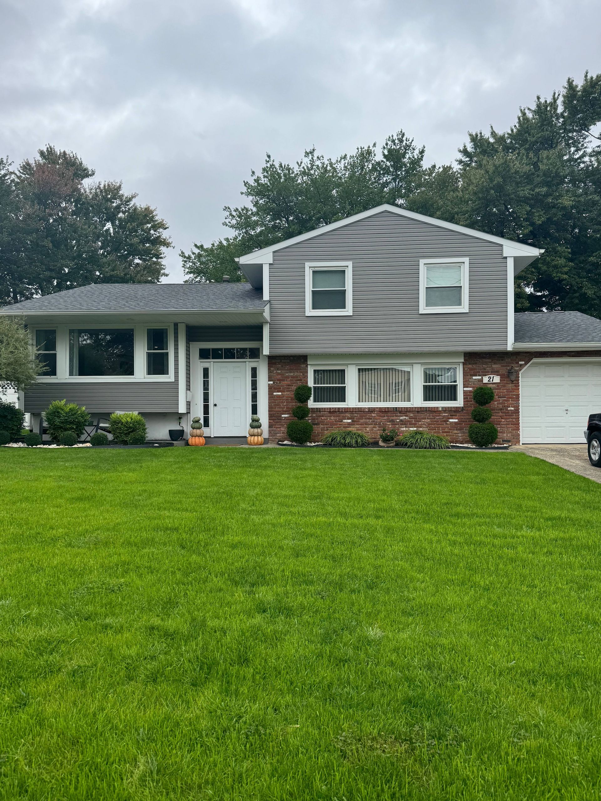 Suburban house with gray siding, white trim, and a large green lawn under a cloudy sky