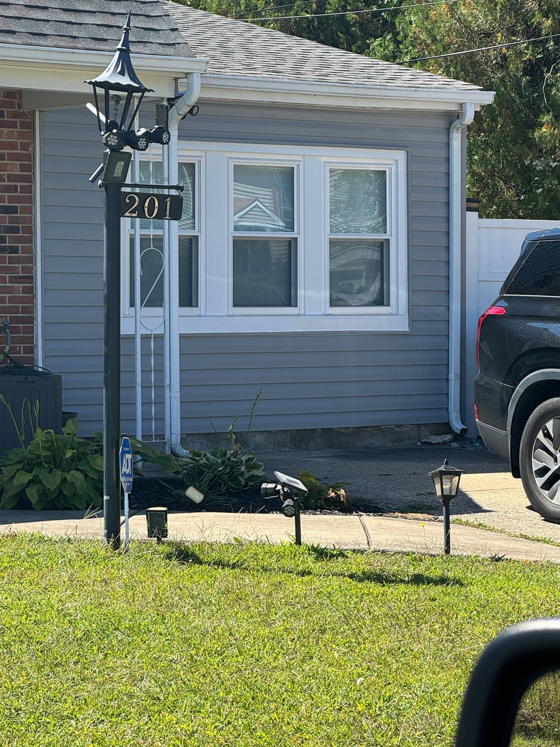 Front of a gray house with a lantern post and the number 207, beside a parked black SUV.