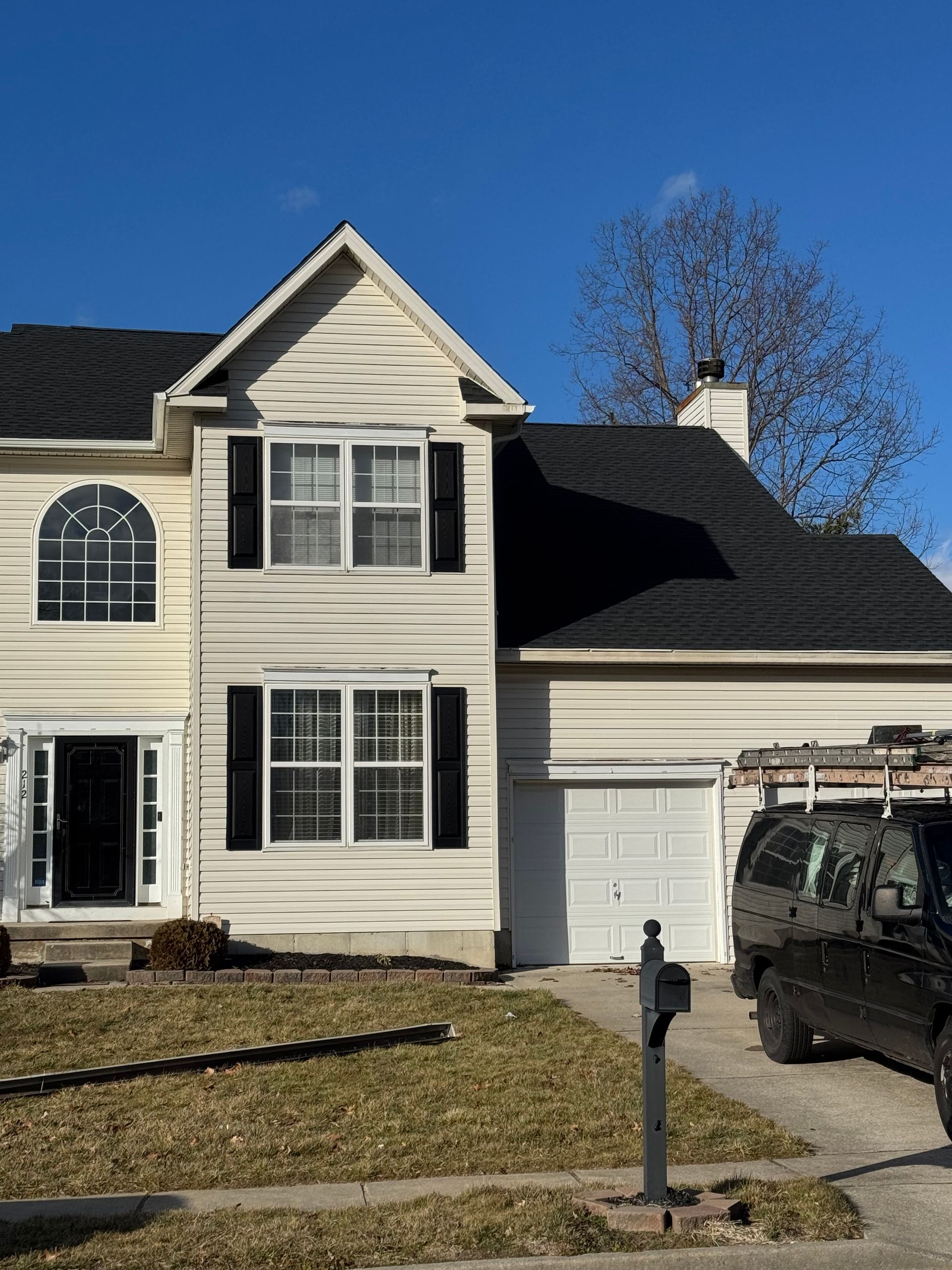 Two-story cream house with black shutters and garage under a clear blue sky