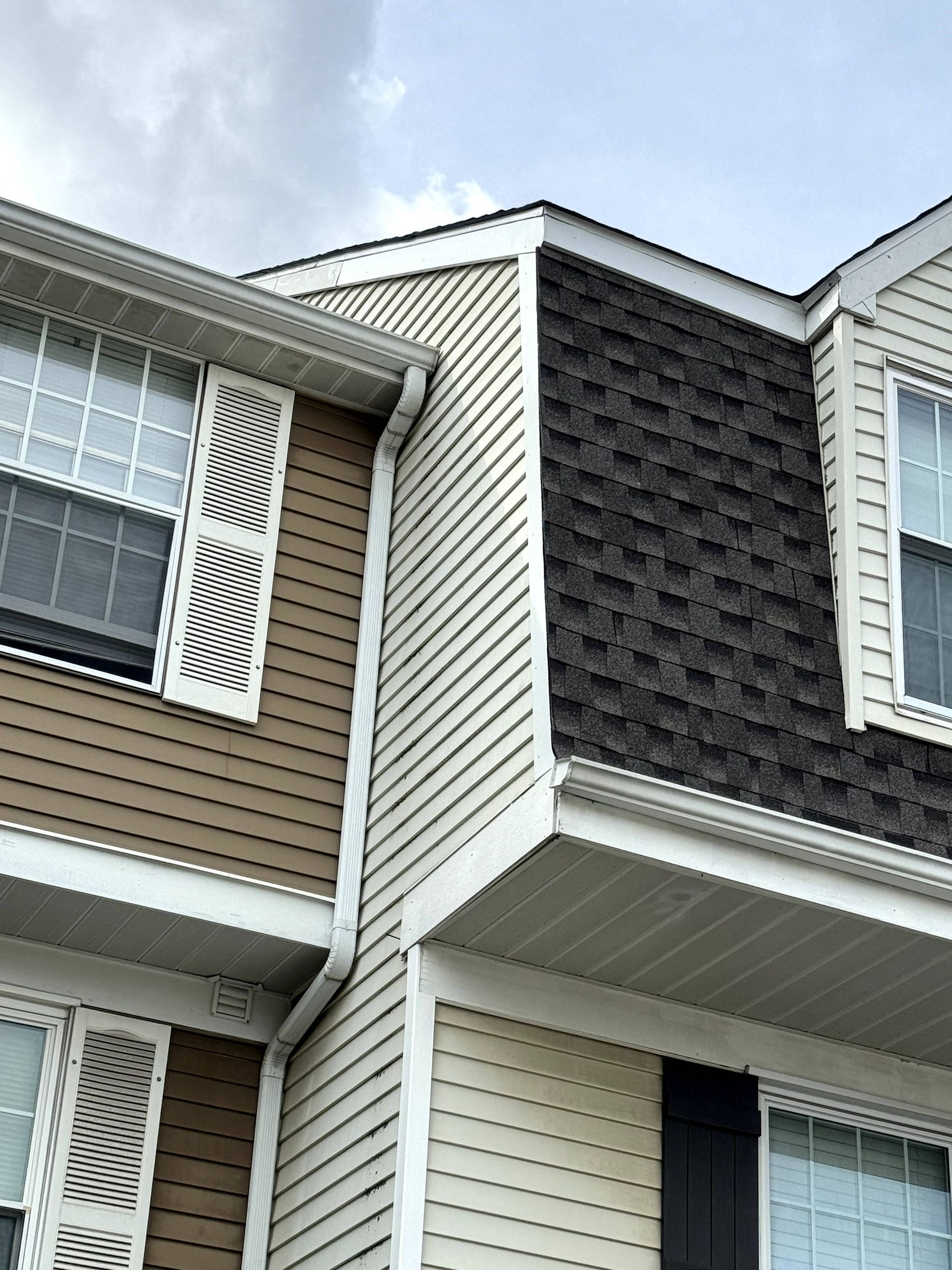Close-up of townhouse siding and shutters with black shingle roof against a blue sky