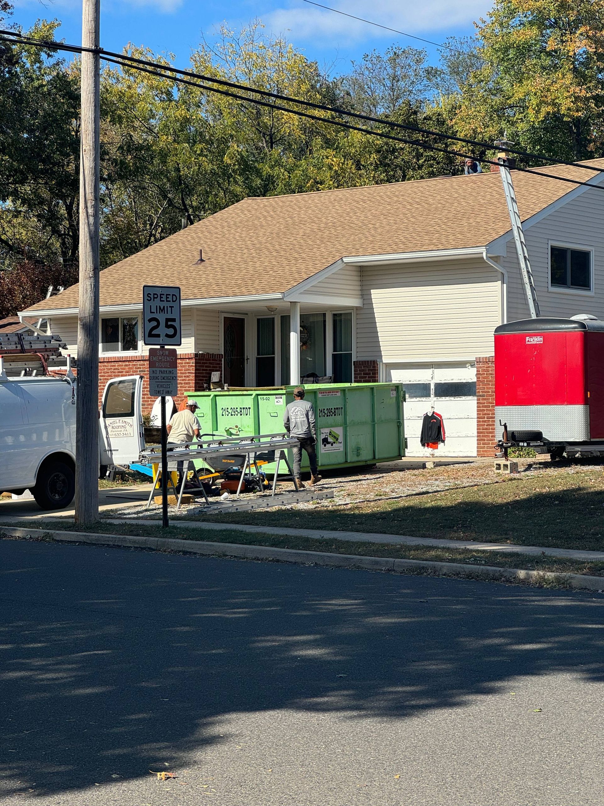 Single-story house with tan roof, green bins, white truck, and red trailer by a roadside speed limit sign.