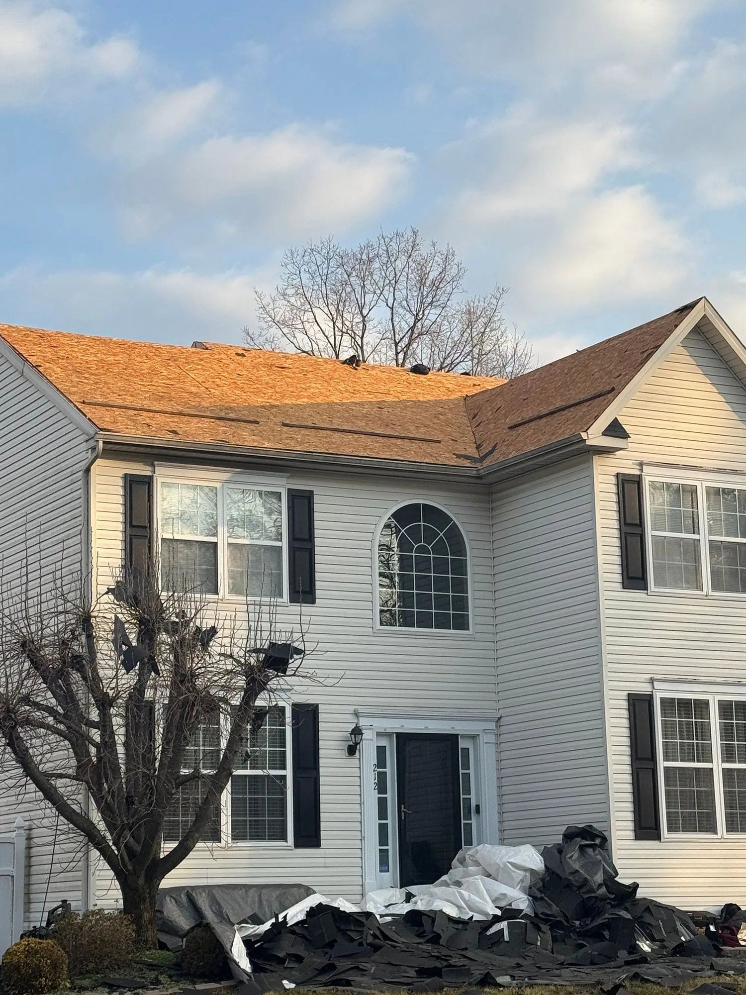 Two-story white house with orange roof and damaged front porch covered in debris