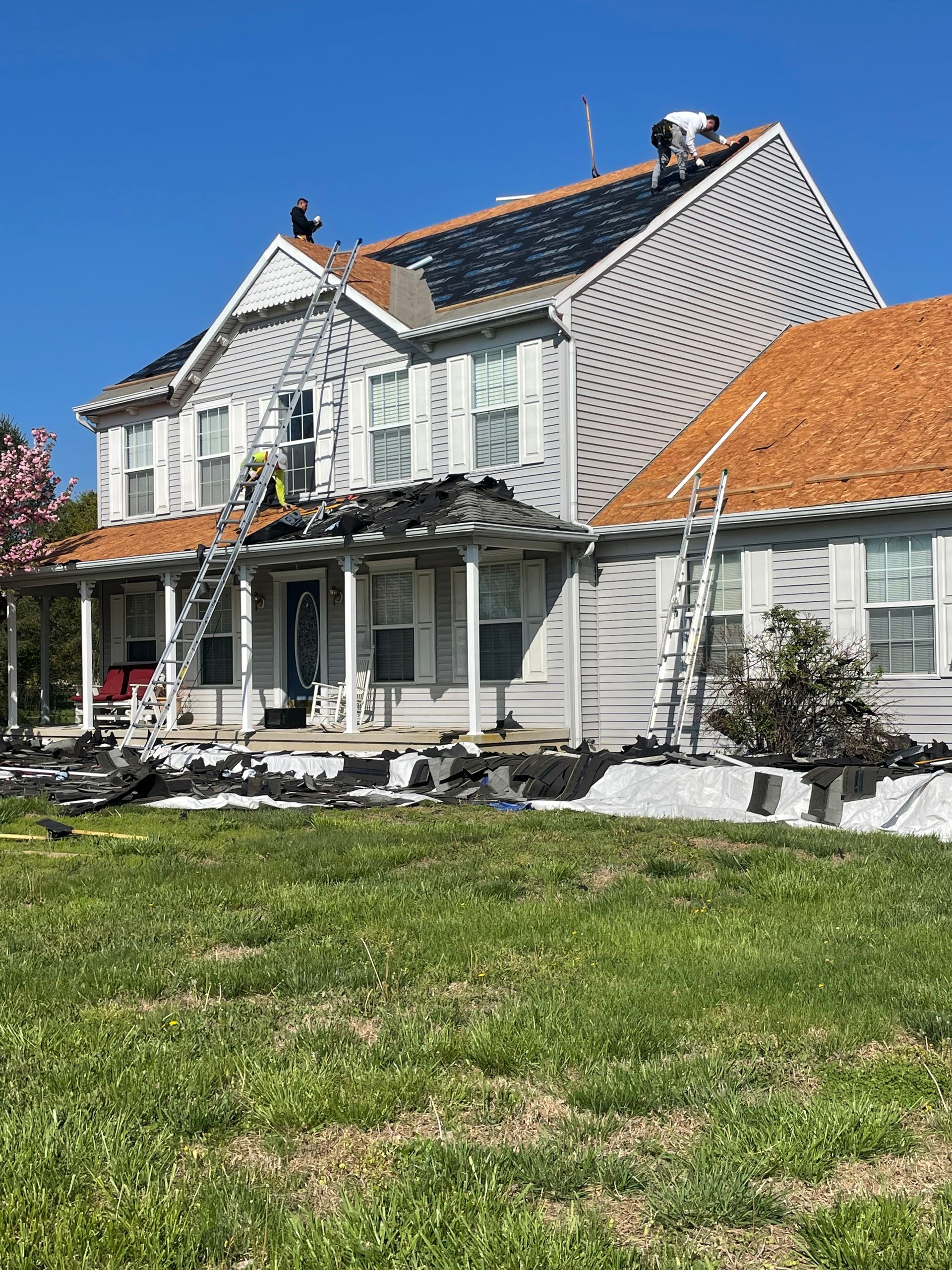Two-story white house with damaged porch, red-tiled roof, and green lawn under a blue sky