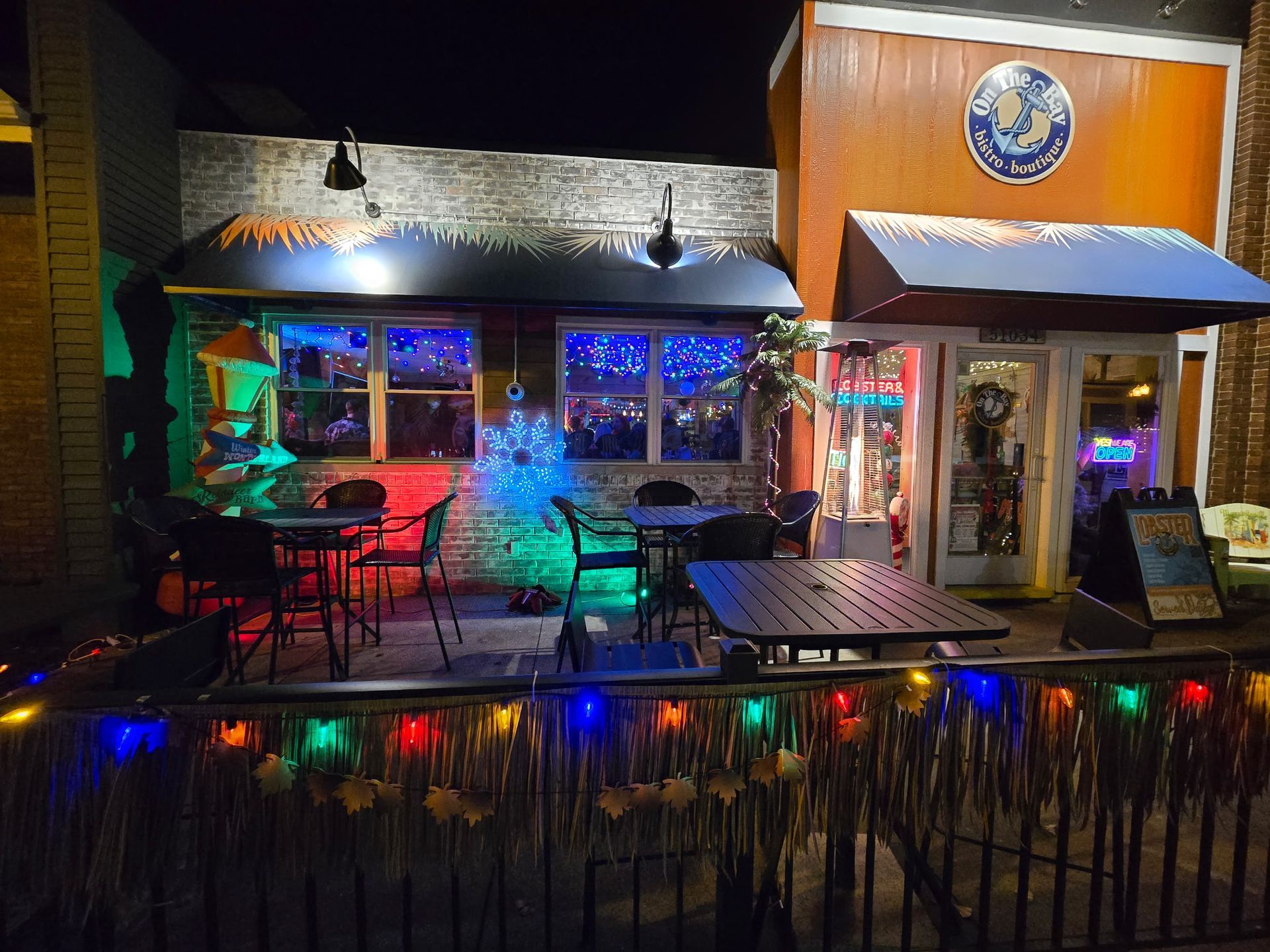 Restaurant facade with blue accents, outdoor seating, and a neon sign at dusk.