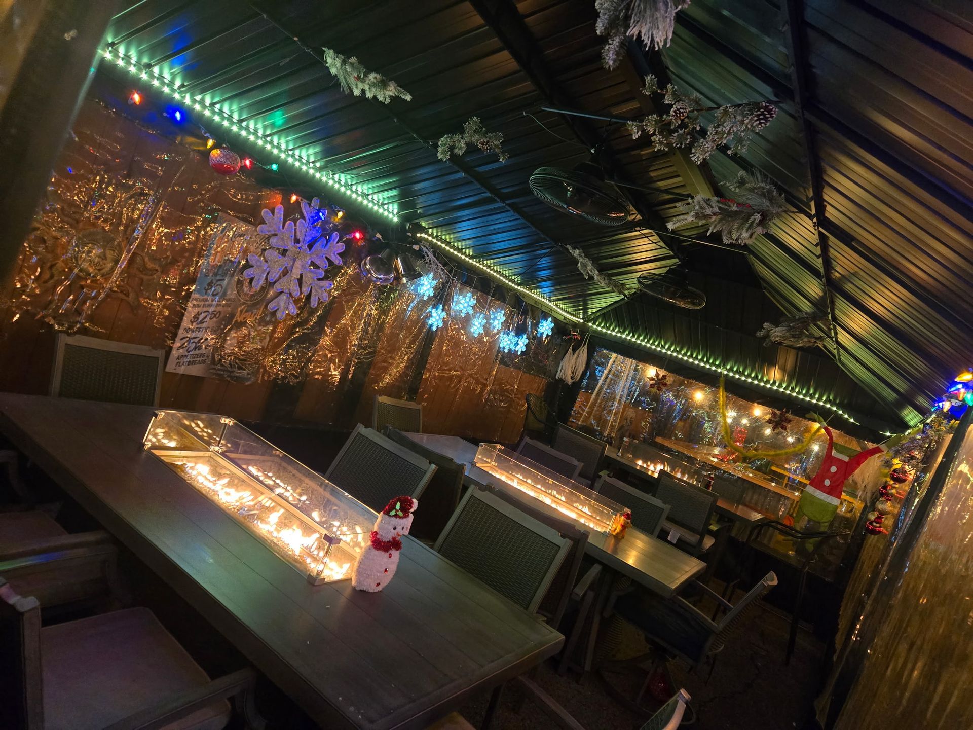 A festive, dimly lit covered outdoor seating area decorated with gold curtains, snowflakes, and holiday string lights.