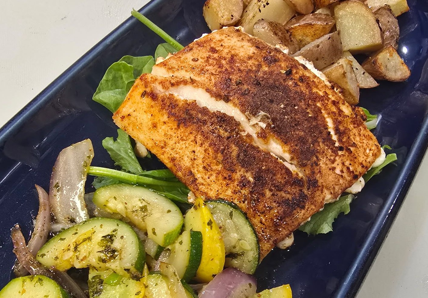 Salmon fillet with roasted potatoes and vegetables on a blue plate.