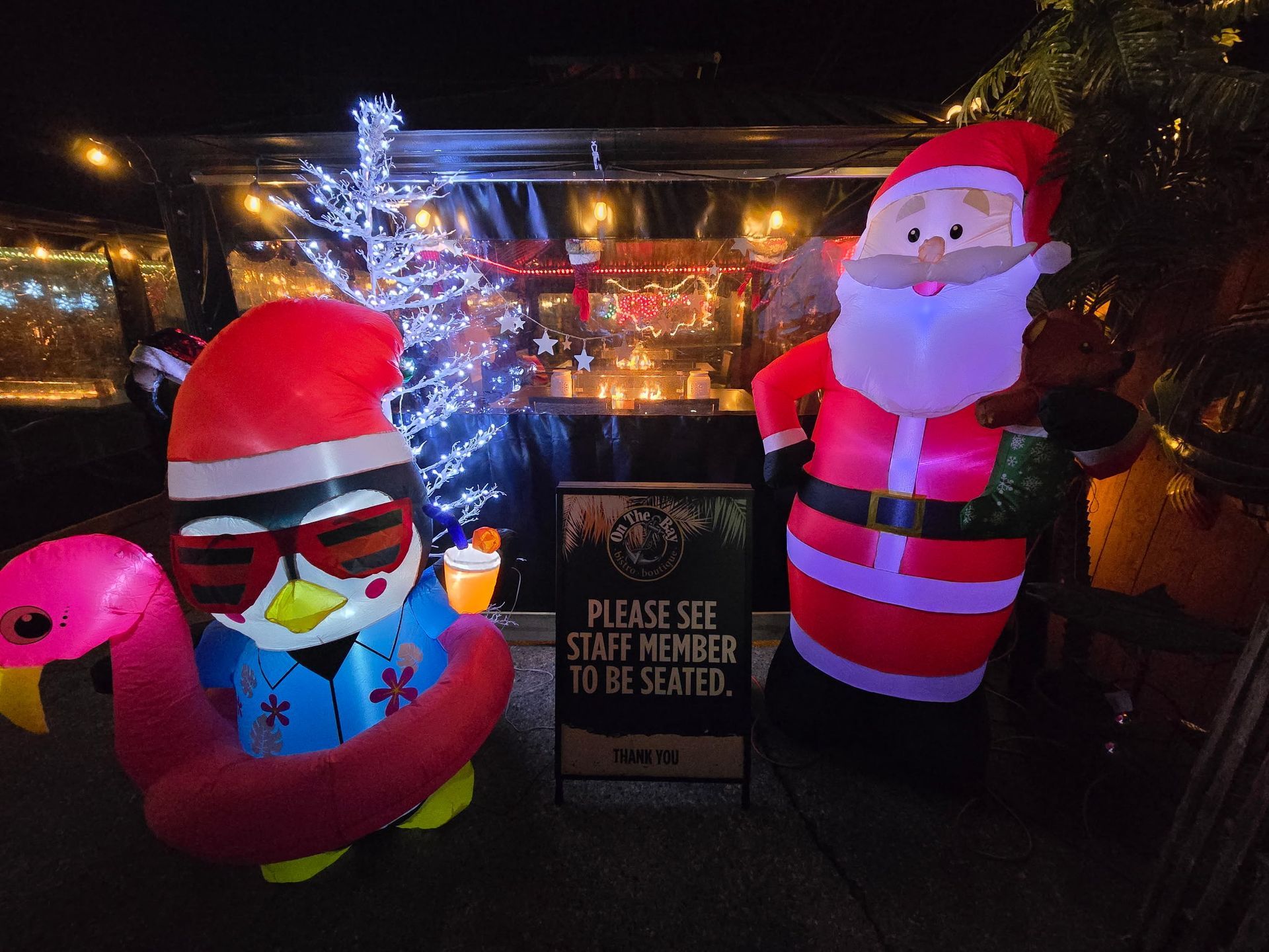 Inflatable Santa, penguin with flamingo floaty, and a sign that reads 