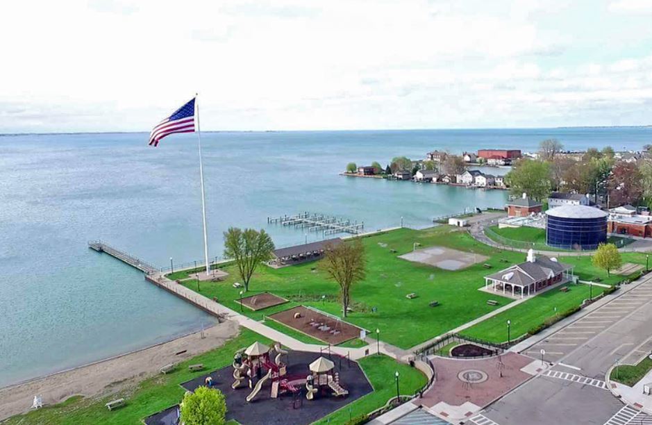American flag flies over a waterfront park, lake in background, buildings dotting the far shore.