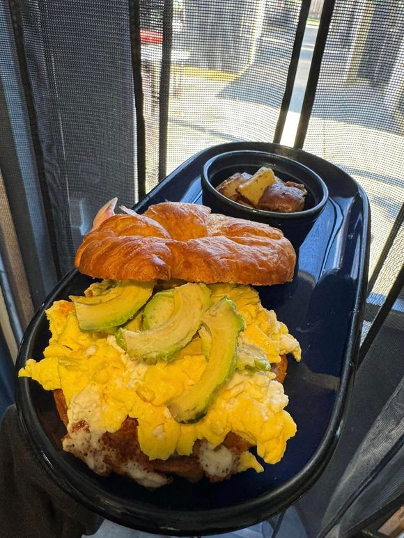 Croissant breakfast sandwich with avocado, scrambled eggs, and a side of fruit or potato at On The Bay Restaurant