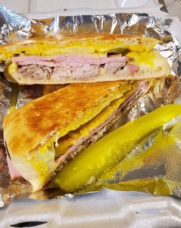 Cuban sandwich, pressed and cut open, with pickle; served in a foil container.