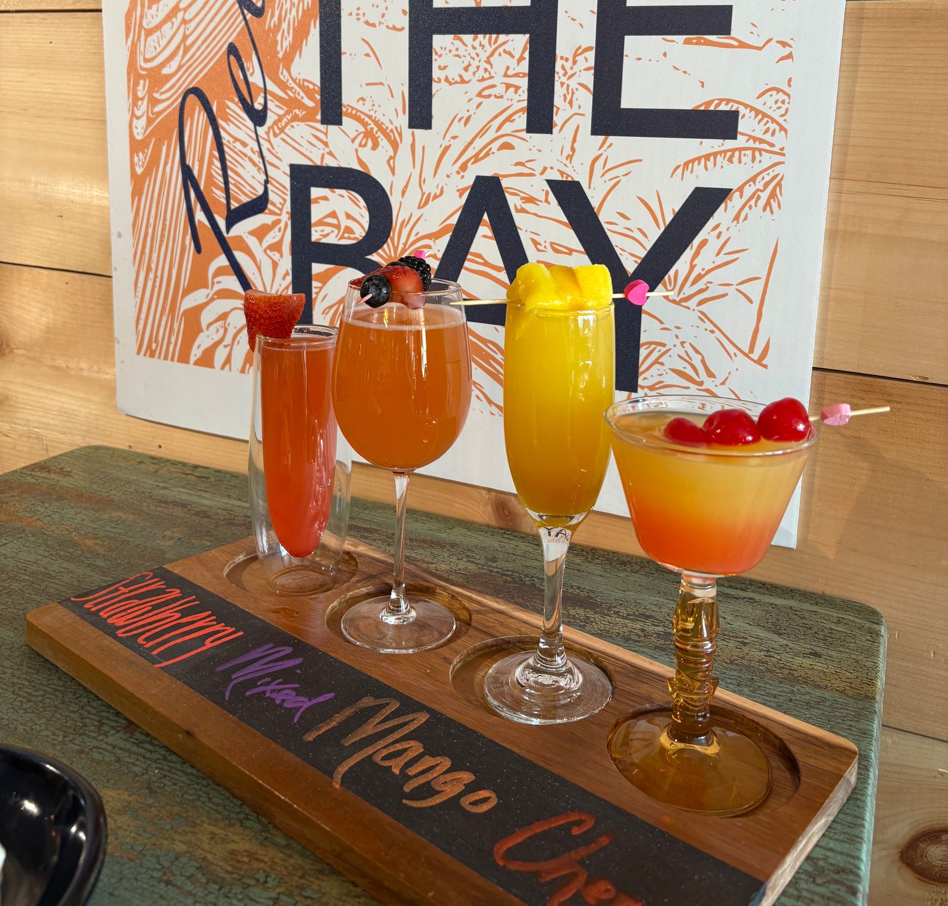 Four colorful cocktails on a wooden tray, with the words 