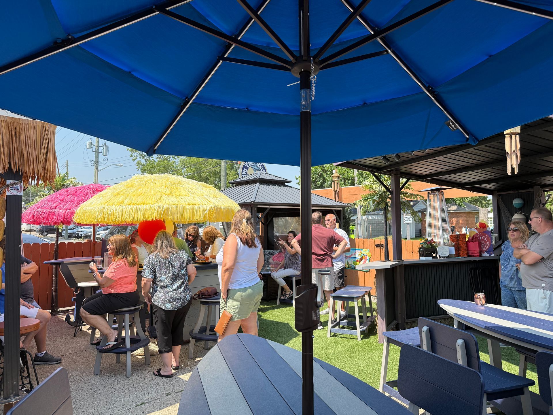 Outdoor patio with people under umbrellas, bar, tables, and grass.