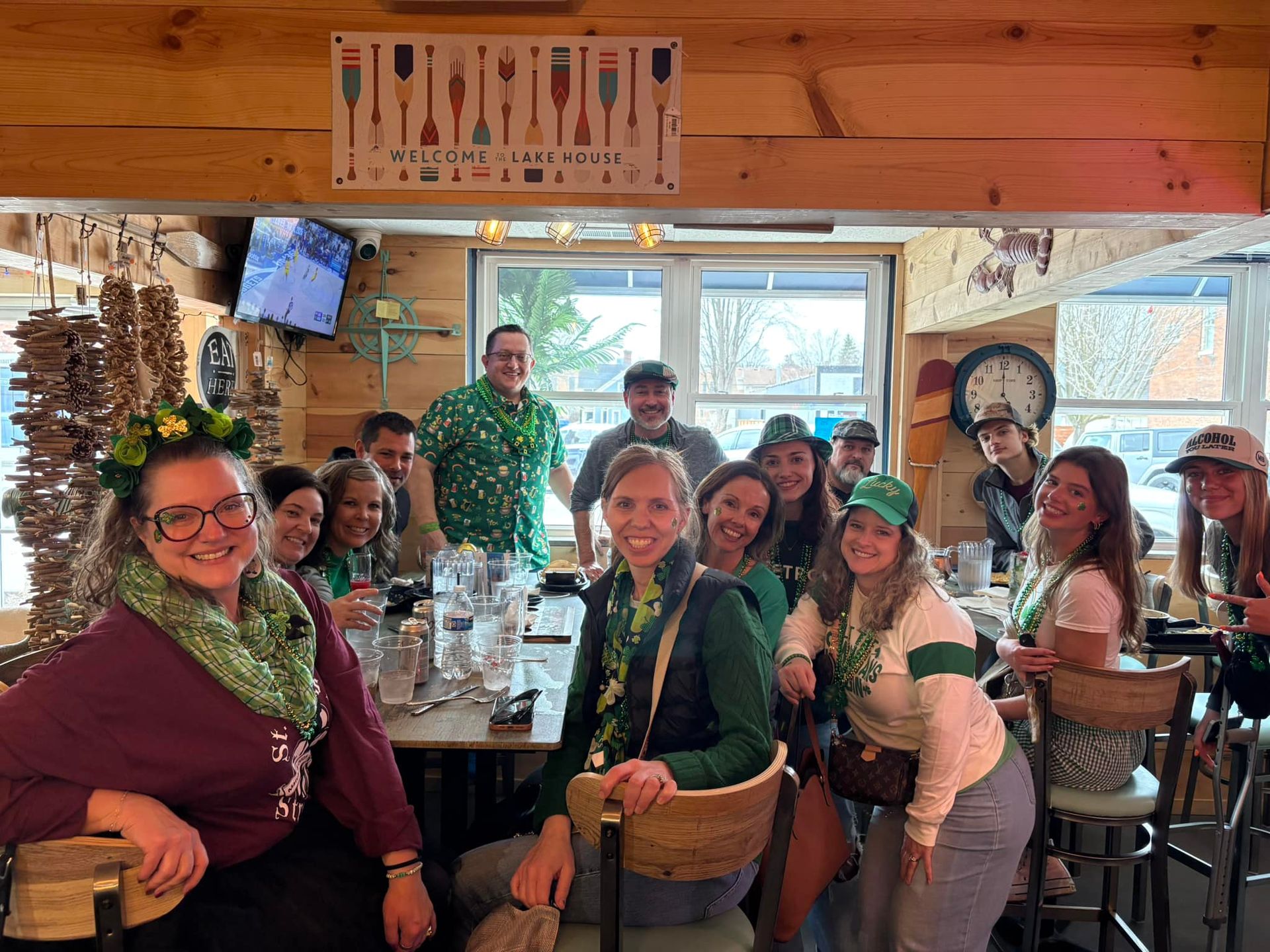 Group of people celebrating St. Patrick's Day in a bar, wearing green, smiling, and enjoying drinks.
