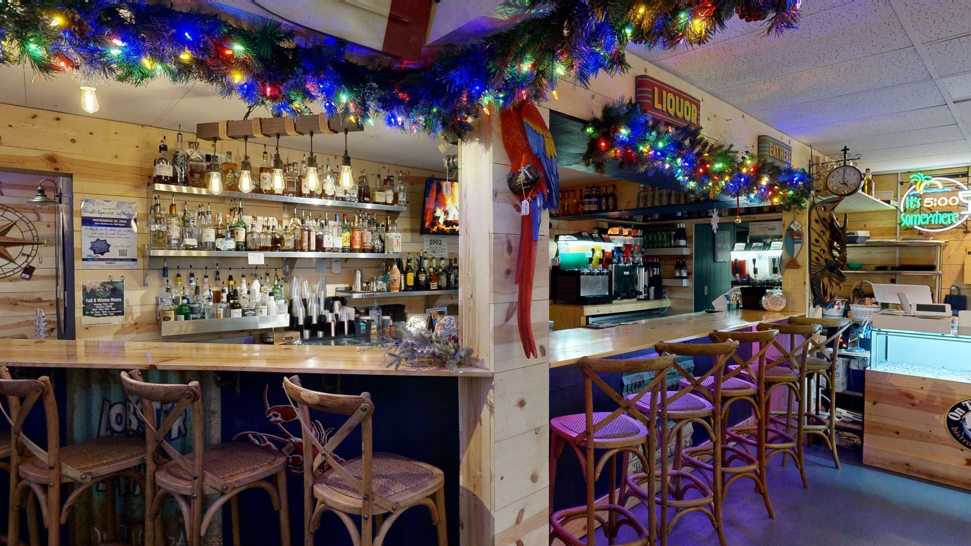 Bar interior with Christmas decorations; wooden bar, stools, and shelves with bottles.