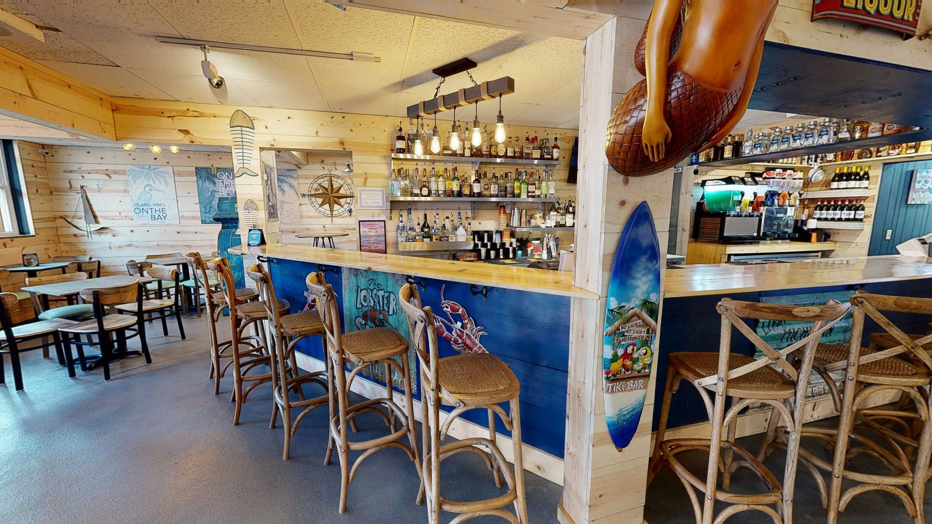 Interior of a beach-themed bar with bar stools, a bar, tables, and decorative surfboards.