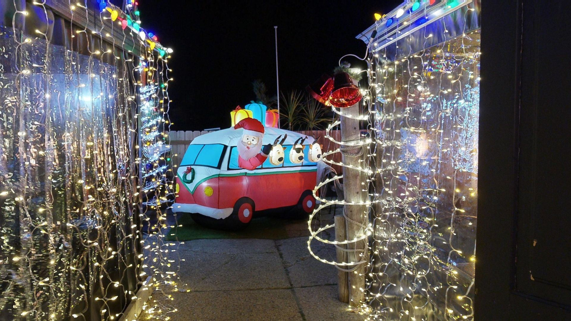 Christmas lights frame a path to a red van decorated as Santa's sleigh with penguin figures inside, presents on top.