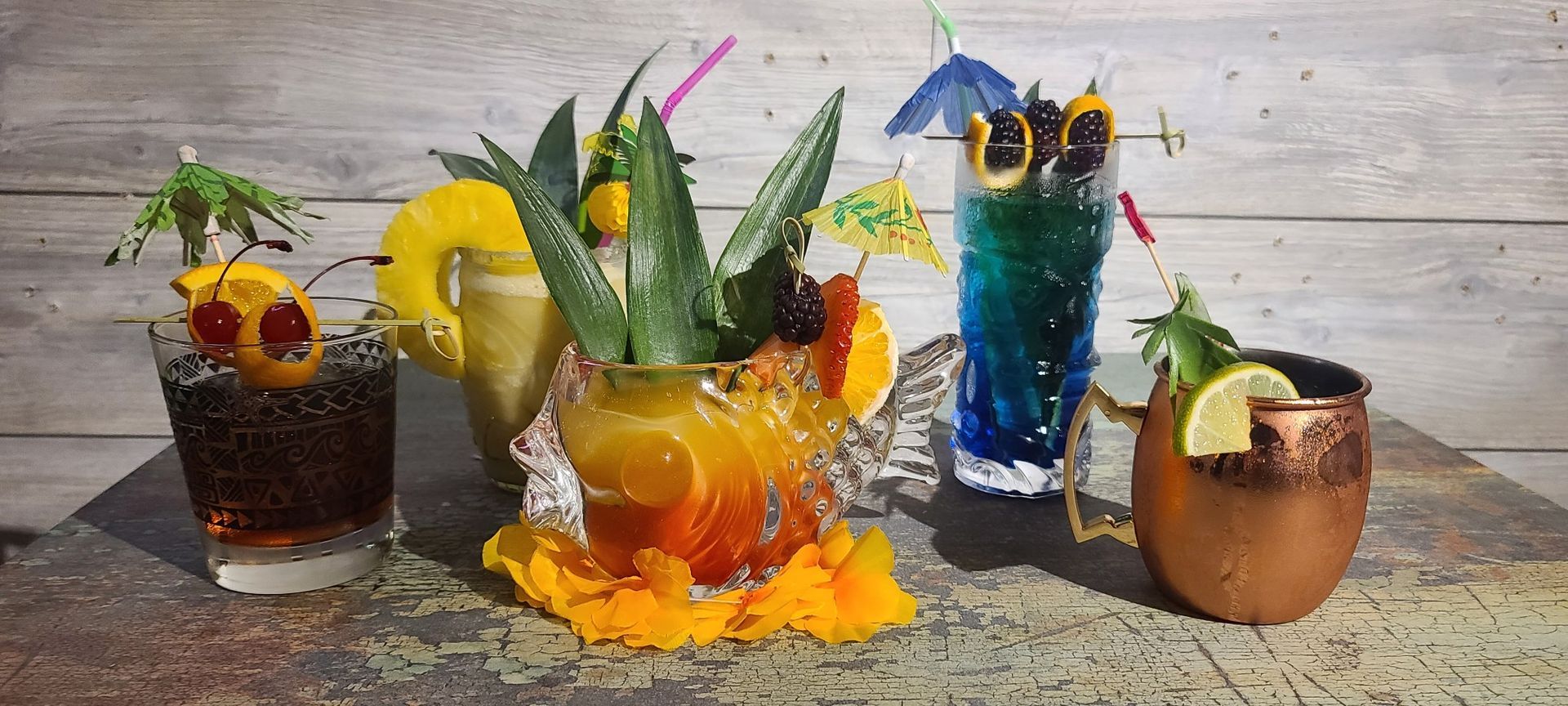 Tropical cocktails in decorative glasses with garnishes on a wood background.