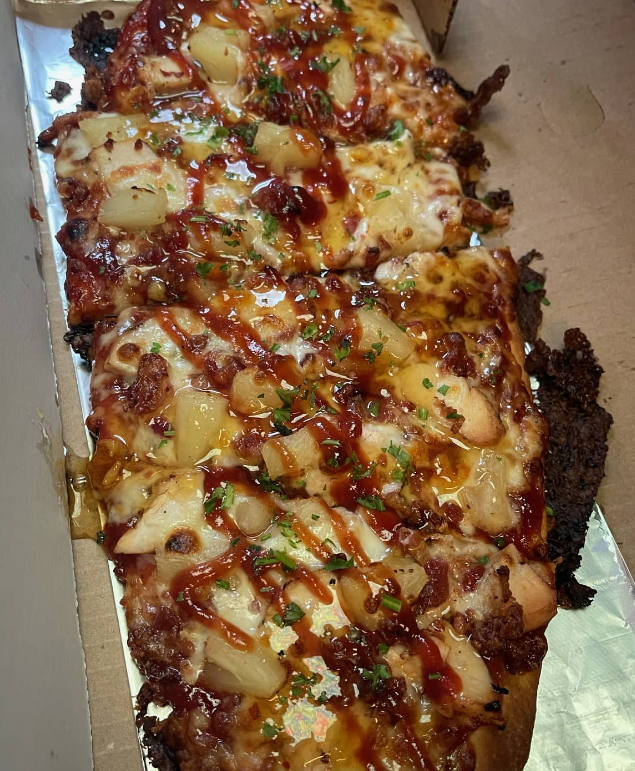 Rectangular pizza slices with pineapple, sauce, and cheese in a to go box at On The Bay restaurant