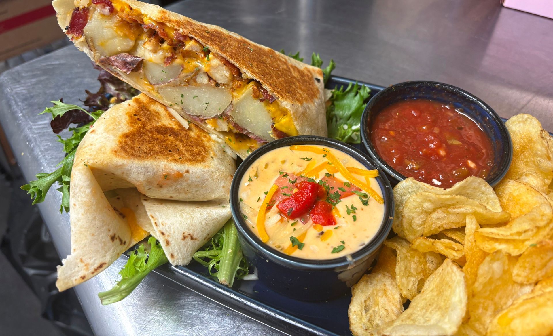 Grilled Cuban sandwich with chips and two dipping sauces on a black platter.