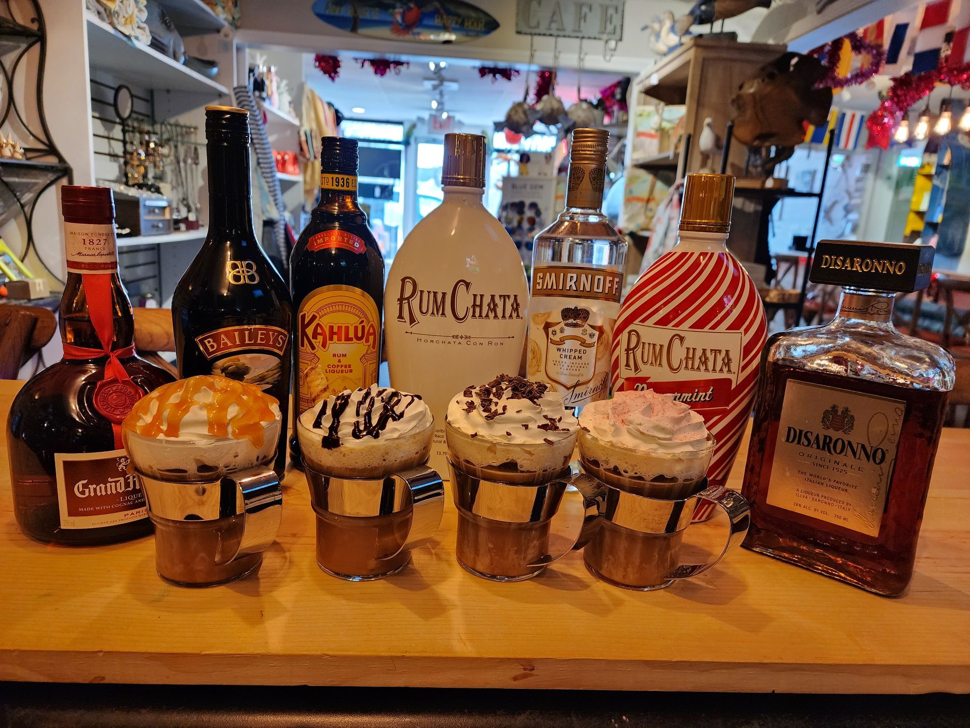 Drinks with whipped cream on bar, bottles of liquor in background, café setting.