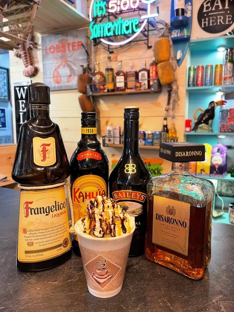 Bottles of Frangelico, Kahlua, Baileys, and Drambuie with a coffee drink in a bar setting.