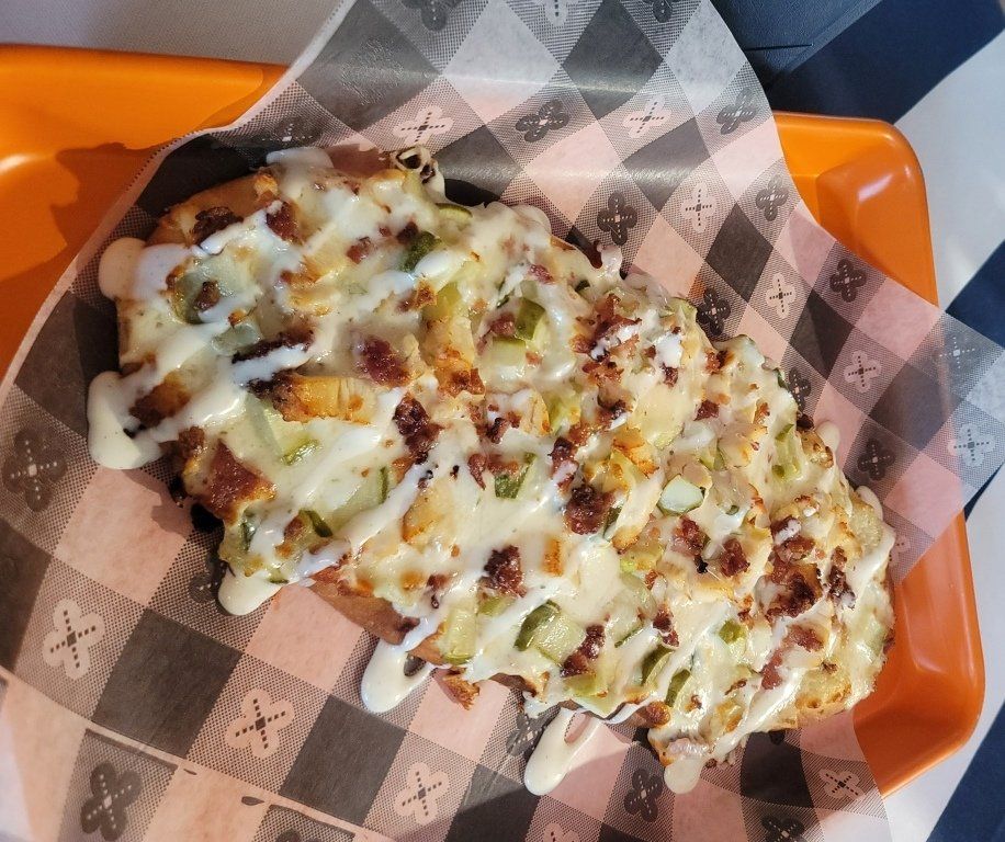 Savory waffle topped with bacon, peppers, and creamy sauce on checkered paper in an orange tray.
