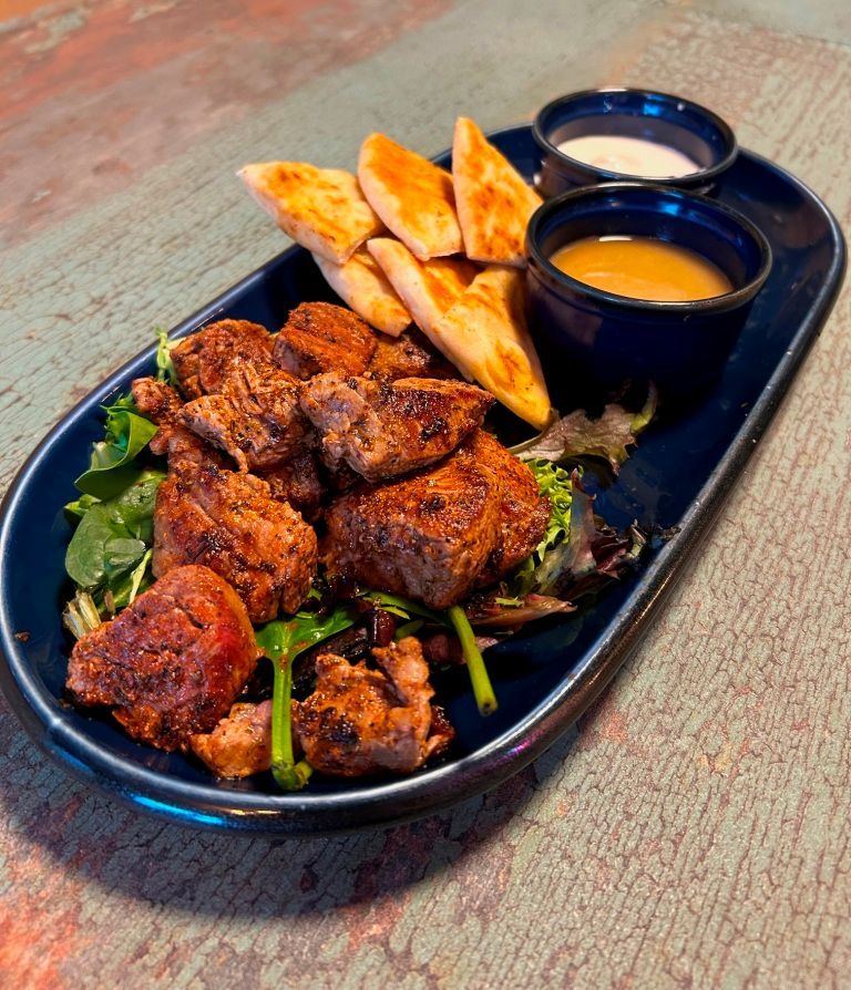 Plate of fried meat cubes, pita bread, and dipping sauces on a blue platter.