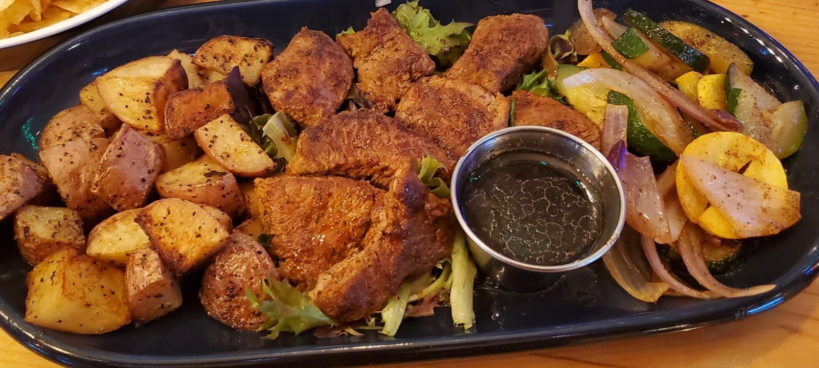 Platter of seasoned fried chicken, potatoes, and onions with a small cup of dipping sauce