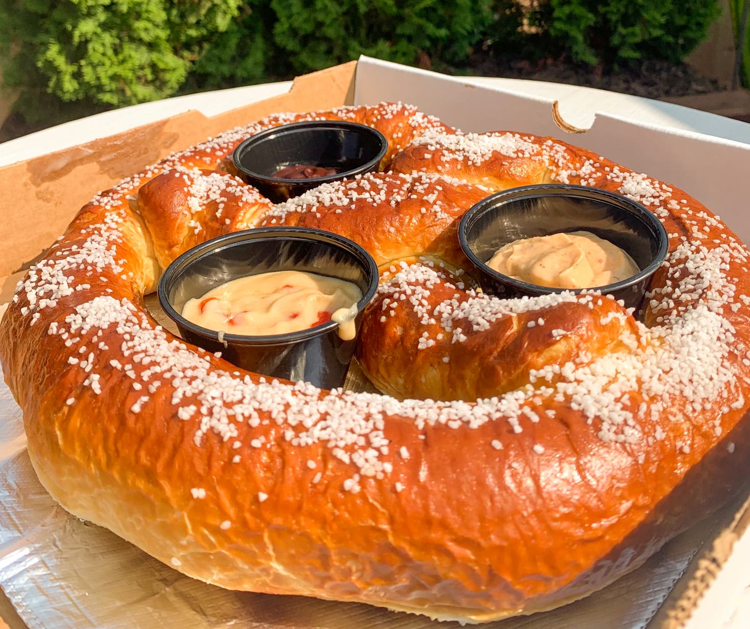 Giant pretzel with three dipping sauces in black containers.