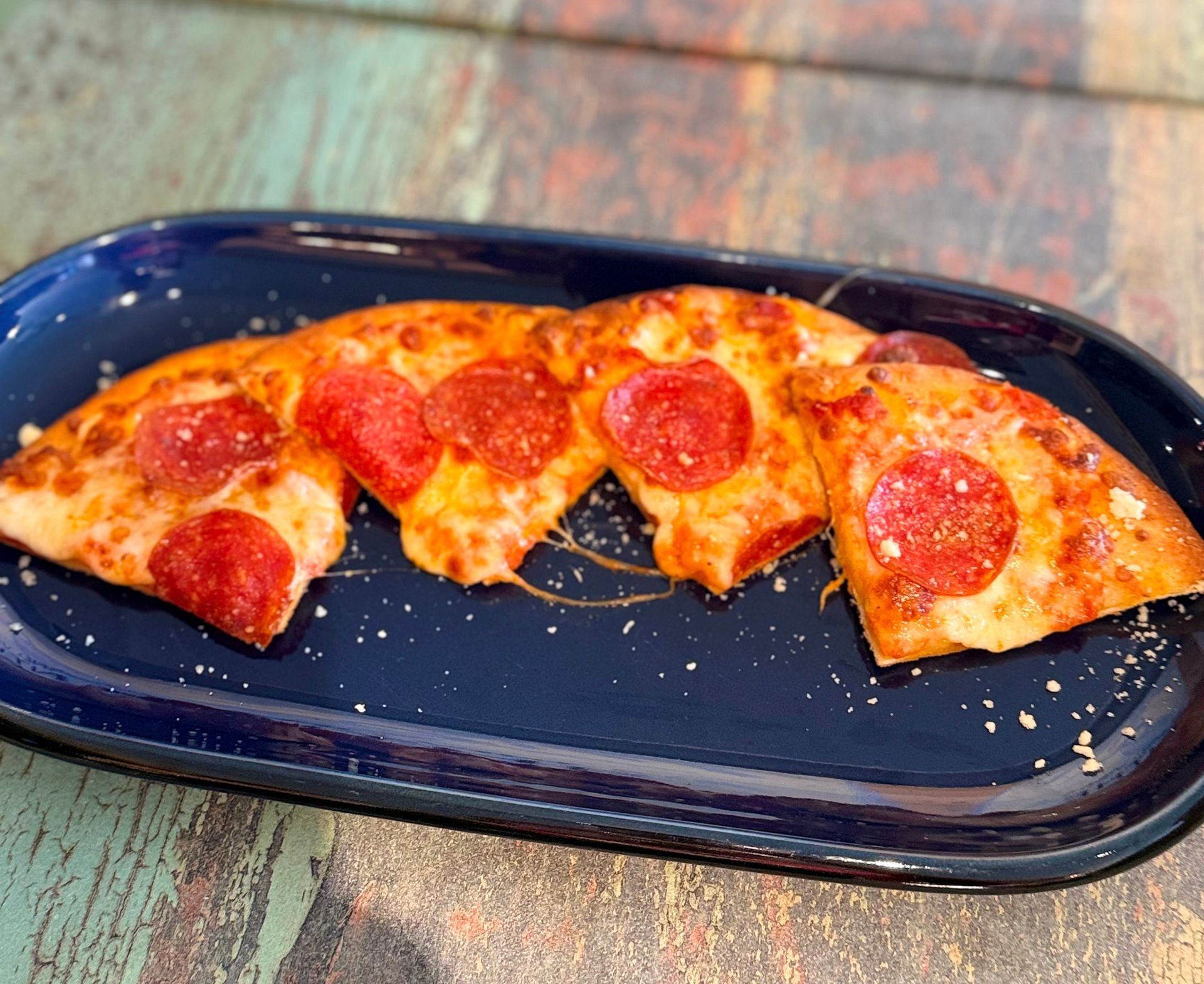 Pepperoni pizza slices on a blue oval plate, on a worn, textured wooden surface.