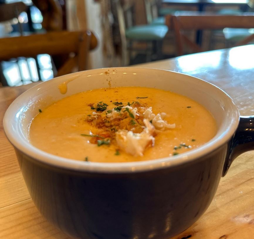 A bowl of orange soup with crabmeat garnish, on a wooden table, indoors.