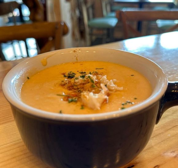 A bowl of creamy orange soup topped with crab meat and herbs on a wooden table.