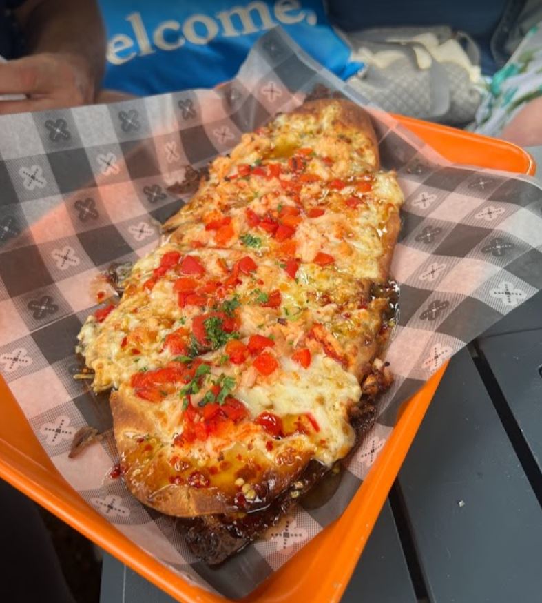 Garlic bread topped with melted cheese and red peppers in an orange basket on a checkered paper.