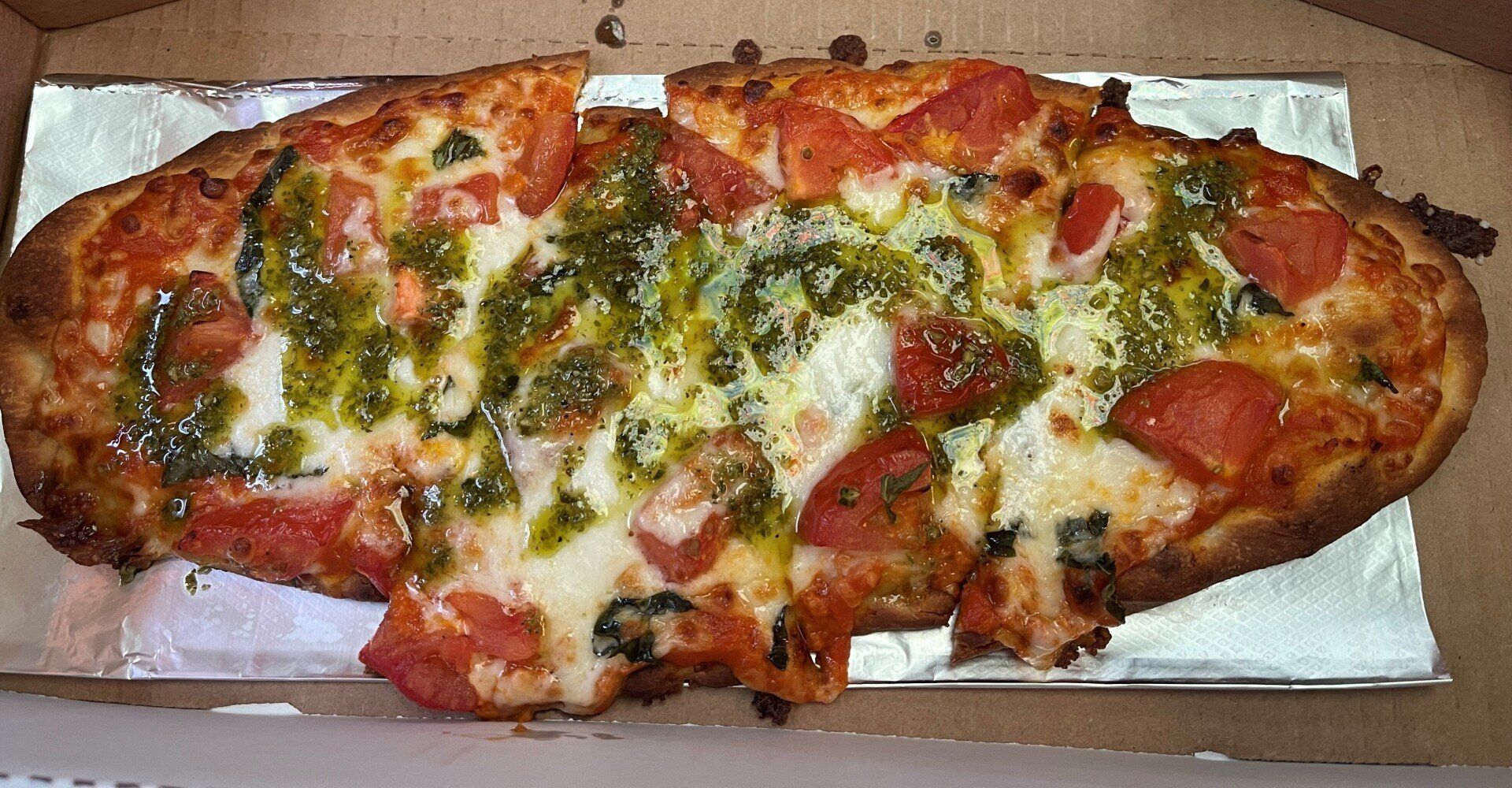 Pizza in a box, topped with pesto, pepperoni, and cheese, cut into slices.