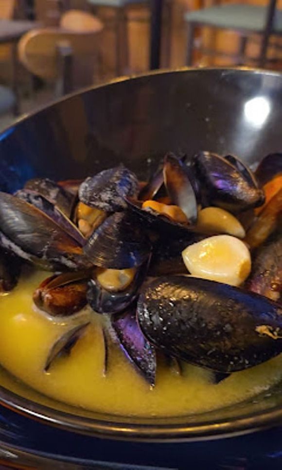Mussels in a yellow broth, served in a dark blue bowl.