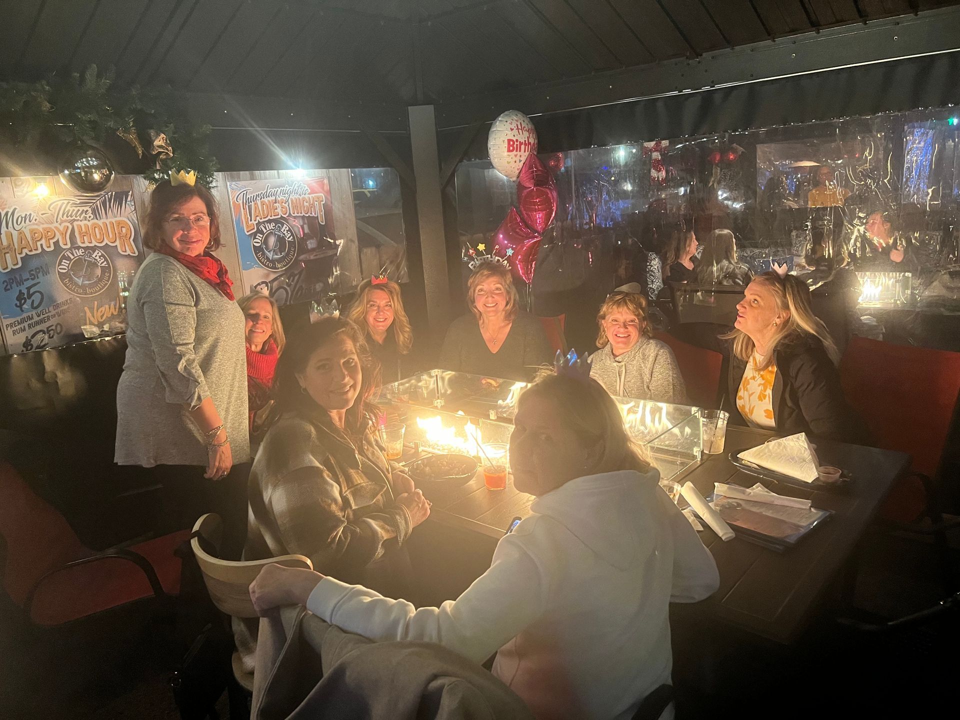 Group of women seated around a fire pit, in a dimly lit outdoor setting.
