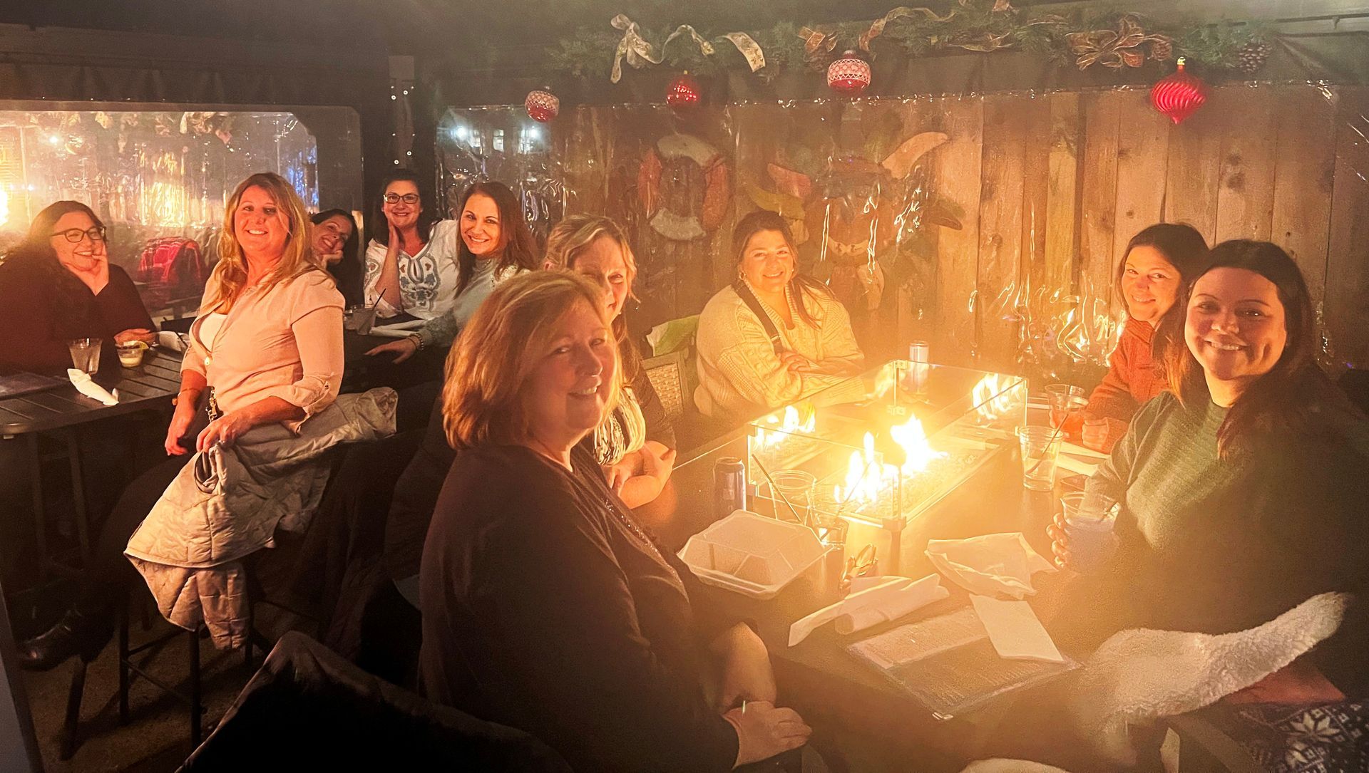Group of women gathered around a fire pit at an outdoor bar, smiling and talking.