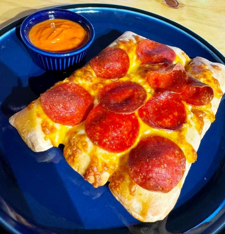 Pepperoni pizza slice with dipping sauce on a blue plate.