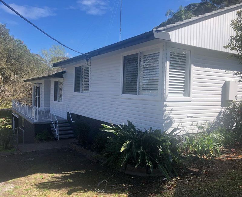 A White House With a Balcony and Stairs is Surrounded by Trees and Bushes  — The Big Bearded Painter In Maitland, NSW