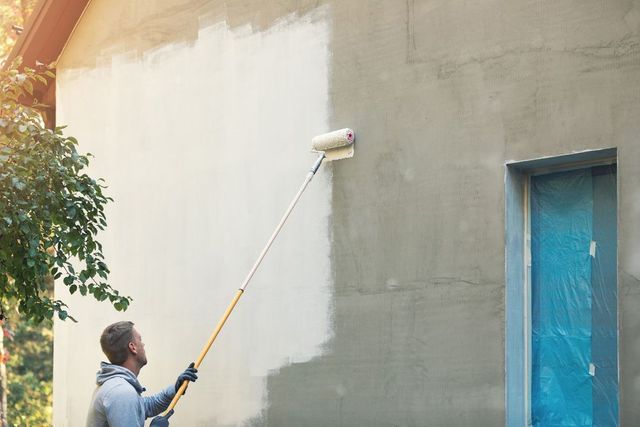 A Man is Painting a Wall With a Paint Roller — The Big Bearded Painter In Kurri Kurri, NSW