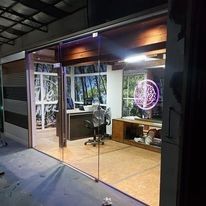 Oficina con fachada de cristal por la noche, con un escritorio, una silla y un letrero de neón rosa en el interior.