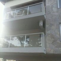 Fachada de un moderno edificio de apartamentos con balcones de cristal y exterior de piedra bañado por la luz del sol.