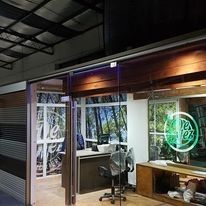 Pequeña tienda moderna con paredes de cristal, escritorio, silla y un letrero de neón verde en la ventana interior.
